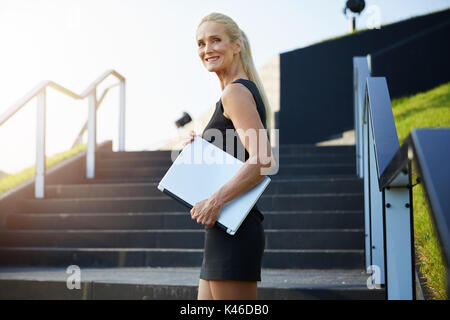 Portrait von Happy Geschäftsfrau auf Treppen holding Laptop. Stockfoto