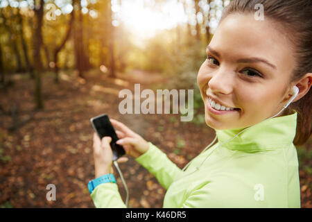 Close up Portrait von ziemlich glücklich sporstwoman wählen Wiedergabeliste auf dem Handy. Stockfoto