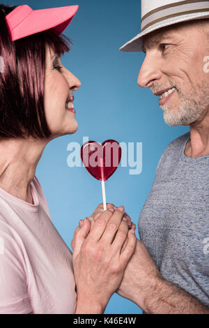 Stilvolle älteres Paar Hände mit Lollipop in Form von Herzen isoliert auf Blau Stockfoto