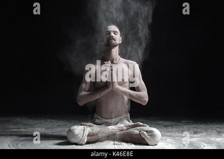 Ein Yoga Lehrer sitzt in einem sukhasana auf schwarzem Hintergrund. Stockfoto