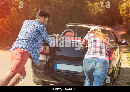 Freizeit, Reise, reisen und Menschen Konzept - glückliche Freunde drücken gebrochen Cabriolet Auto auf Landstraße Stockfoto