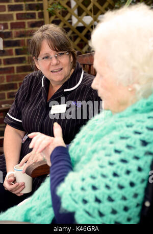 Community Hospital Matrone in Kaffee und ein Schwätzchen mit älteren Patienten im Krankenhaus Garten, Haslemere, Surrey, Großbritannien. 01.09.2017. Stockfoto