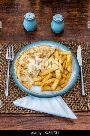 Omelette und gewellter schneiden Sie die Kartoffeln abbrach, auf einem denby Steingut Teller, mit begleitenden Servietten, Salz- und Pfefferstreuer, Edelstahl Messer und Gabel. Stockfoto