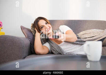 Porträt der jungen Frau bequem auf der Couch wechseln der Kanäle im TV. Stockfoto