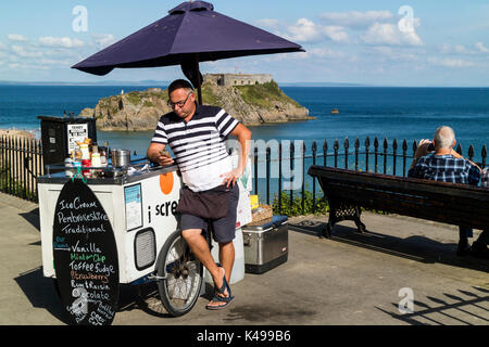 Ein Mann verkaufen Eis von einem Fahrrad am Meer in Tenby, Wales prüft seine Mobile/Handy mit St Catherine's Insel im Hintergrund Stockfoto