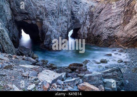 An der Basis der Dungeon in den Kerker Provincial Park sind zwei Bögen an der Unterseite einer Spüle Loch bei Sonnenaufgang in Neufundland, Kanada. Stockfoto