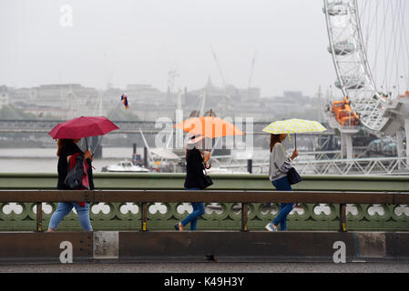 Frauen, die die Westminster Bridge überqueren, gehen mit hellen Regenschirmen im Regen in London, Großbritannien Stockfoto