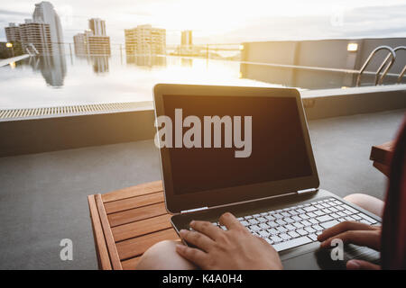 Ein Mann mit Computer, Laptop, Sonnen Lounge Chair am Schwimmbad in der Stadt, selektive konzentrieren. Beschneidungspfad Bildschirm Stockfoto