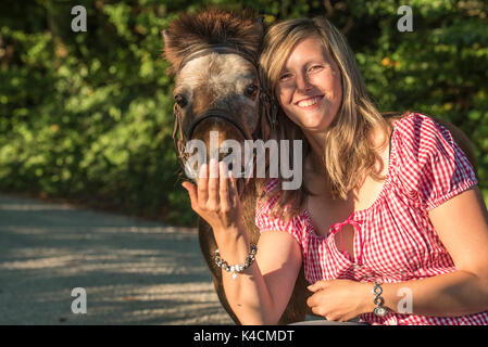 Lachende junge blonde Frau quält Brown Shetland Pony Stockfoto