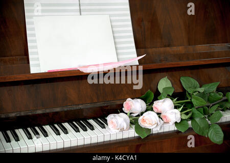 Piano, Blumenstrauß aus fünf Blassrosa Rosen am Keyboard, Musik und weißen, leeren Blatt Papier mit rosa Feder. Stockfoto