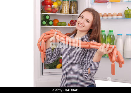 Junges Mädchen hält Würstchen auf dem Kühlschrank Hintergrund. Schöne junge Mädchen in der Nähe der Kühlschrank. Stockfoto