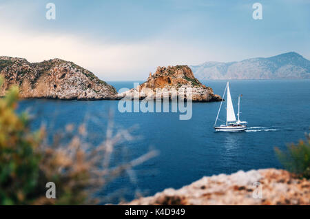 Segelboot mit deutscher Flagge segeln im Mittelmeer zwischen Felsen und Steinen gegen die stürmischen Himmel, Santa Ponsa, Mallorca, Spanien Stockfoto