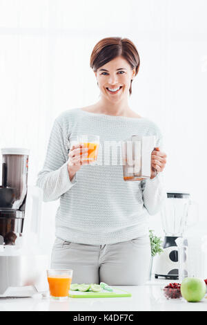 Lächelnden jungen Frau Vorbereitung gesunde Getränke mit frischem Gemüse und Früchten, sie ist mit einem Entsafter Stockfoto