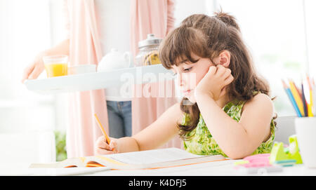 Süße Mädchen studieren zu Hause, ihre Mutter bringt ihr einige gesunde Snacks, Familie und Lifestyle Konzept Stockfoto