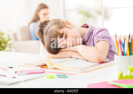 Faule Schüler Mädchen schlafen auf ihre Bücher, ihre Mutter saß auf dem Sofa, auf dem Hintergrund ist Stockfoto
