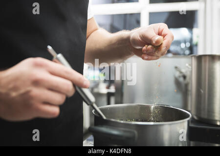 Nahaufnahme auf Koch Hände gießen Gewürze in die Suppe Stockfoto