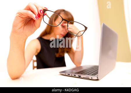 Müde und gestresst. Frustrierte junge Frau hält die Augen geschlossen und massieren Nase, während an Ihrem Arbeitsplatz im Büro Stockfoto