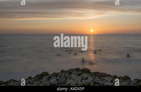 Sonnenuntergang über dem Wasser zu Plage L'Amelie, in der Nähe von Soulac-sur-Mer, mit Surfer bewegen im Wasser (lange Belichtung). Stockfoto