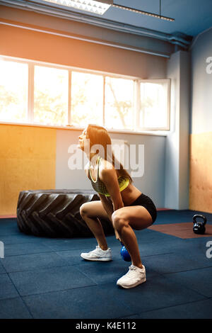 Sportliche Frau Training mit Wasserkocher Glocke während man in die Hocke. Stockfoto