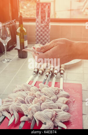 Eine Hand Stücke von marinierten Hähnchen am Spieß in der Küche an einem sonnigen Tag. Stockfoto