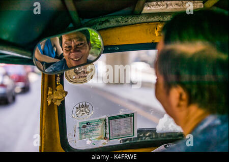 Eine glücklich lächelnde Tuk Tuk Fahrer in seinem Rückspiegel, Bangkok, Thailand gesehen. Stockfoto