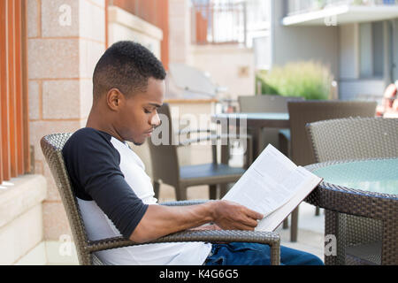 Closeup Portrait, intelligenten jungen Mann mit intensiven Konzentration, hinsetzen und lesen Buch, im freien Hintergrund isoliert. Wissen ist Macht Konzept Stockfoto