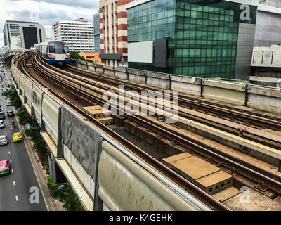 Tagesansicht des elektrischen Sky Zug, der auf die Gleise in der Innenstadt von Bangkok, Thailand mit Verkehr und hohe Gebäude im Hintergrund Stockfoto