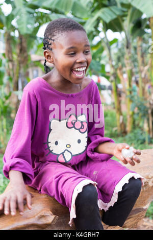 Eine schöne junge Mädchen lächelnd. Sie ist in einem violetten Hello Kitty T-Shirt bekleidet und sitzen auf einen umgestürzten Baumstamm. Stockfoto