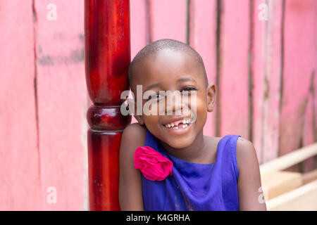 Eine schöne junge Mädchen lächelnd. Sie ist in einem blauen Kleid mit rosa Blume auf der Schulter gekleidet. Stockfoto
