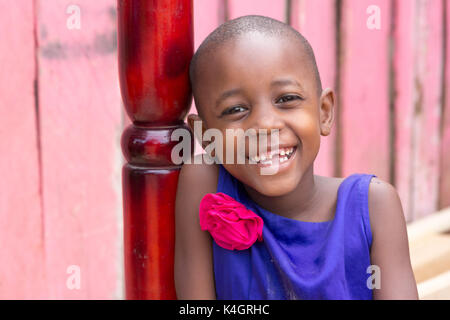 Eine schöne junge Mädchen lächelnd. Sie ist in einem blauen Kleid mit rosa Blume auf der Schulter gekleidet. Stockfoto