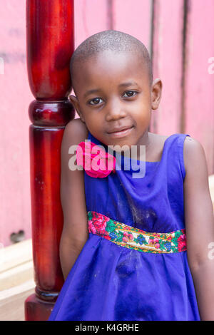 Eine schöne junge Mädchen lächelnd. Sie ist in einem blauen Kleid mit rosa Blume auf der Schulter gekleidet. Stockfoto
