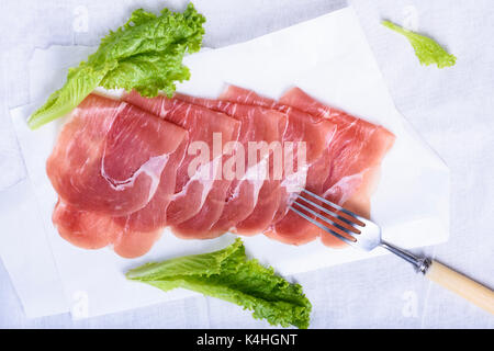 Italienische Prosciutto, kuriert Schweinefleisch Schinken. Geschnetzeltes Fleisch Snack mit Salat. Oben betrachten. Stockfoto