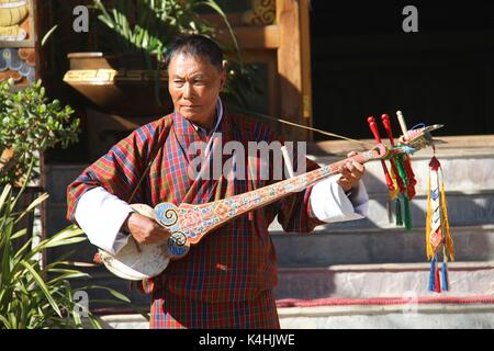 PARO, BHUTAN - November 10, 2012: Unbekannter alter Mann Musiker in traditioneller Kleidung (GHO) spielen Dramnyen Instrument im Hotel in Paro, Bhutan Stockfoto