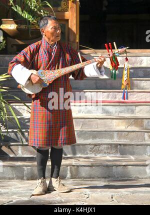 PARO, BHUTAN - November 10, 2012: Unbekannter alter Mann Musiker in traditioneller Kleidung (GHO) spielen Dramnyen Instrument im Hotel in Paro, Bhutan Stockfoto