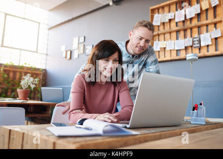 Zwei leger gekleidete junge Kollegen mit einem Laptop und miteinander sprechen, während Sie sich an einer Tabelle steht in einem modernen Büro Stockfoto