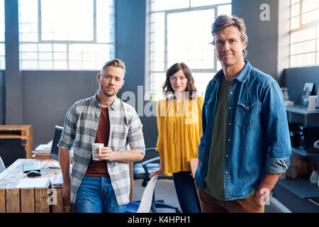 Portrait von drei fokussierte junge Geschäftsleute selbstbewusst lächelnd, während in einer großen modernen Büro arbeiten Stockfoto
