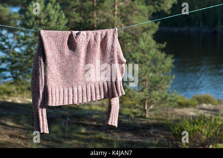 Ein rosa Strickpullover ist das Trocknen auf einem Seil im Wald zwischen den Bäumen. Stockfoto