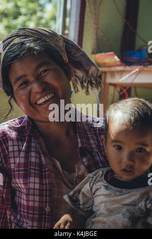 Die Menschen und die malerische Aussicht auf das ländliche Leben in der Landschaft von Myanmar, ehemals Burma bekannt. Hier ein Frauen hält Ihr Baby in Ihrem Haus. Stockfoto