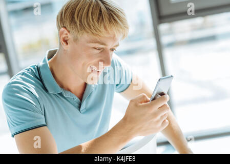 Der blonde Junge Mann mit seinem Smart Phone Stockfoto