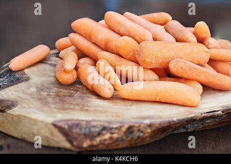 Babykarotten Übereinander einen hölzernen Schneidebrett über eine rustikale Tabelle.. Stockfoto