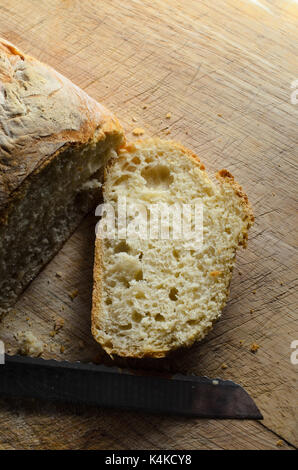 Overhead shot von frisch gebackenem Brot. Erste Scheibe abgeschnitten und liegen bis auf Holz Schneidebrett mit Messer Gesicht. Stockfoto