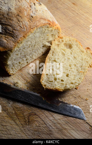 Frisch gebackenes Brot, Schuß von oben. Erste Scheibe abgeschnitten und liegen bis auf Holz Schneidebrett mit Messer Gesicht. Stockfoto