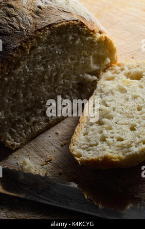 Frisch gebackenes Brot, mit ersten Slice Schnitt und liegen bis auf Holz Schneidebrett mit Messer Gesicht. Stockfoto