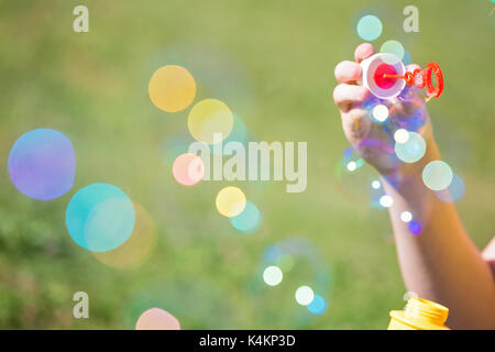 Girl's Hand mit einem Bubble Maker und bläst Seifenblasen, gegen die unscharfe Gras Hintergrund Stockfoto