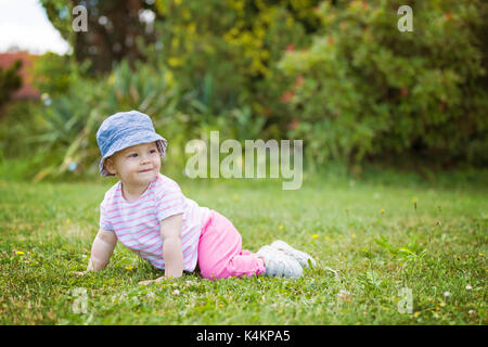 Vierzehn Monate altes Baby Mädchen kriecht auf Gras auf den sonnigen Sommertag Stockfoto