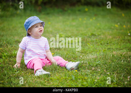 Vierzehn Monate altes Baby Mädchen sitzen auf dem Gras auf der sonnigen Sommertag Stockfoto