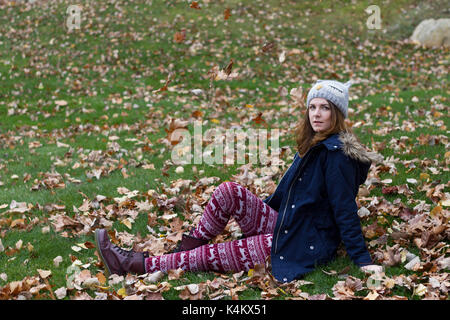 Junge Frau in der Nähe von Blätter in der Natur sitzen. Stockfoto