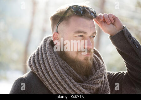 Mann im Winter Mantel und Sonnenbrille im Wald Stockfoto