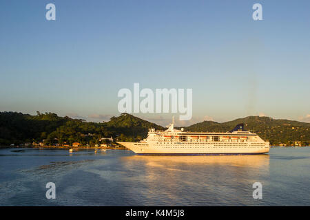 Kreuzfahrtschiff Norwegian Sea günstig bei Coxen Hole aus Roatan, Hondurs, Karibik, im goldenen Abendlicht mit hügeligen Insel Landschaft hinter Stockfoto