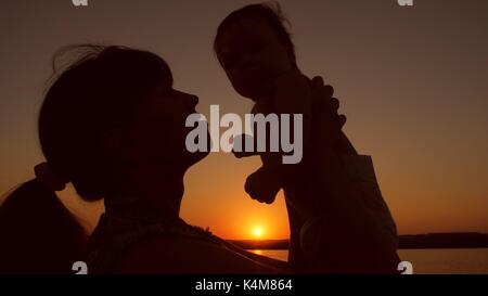 Mutter wirft Baby spielt bei Sonnenuntergang. Stockfoto